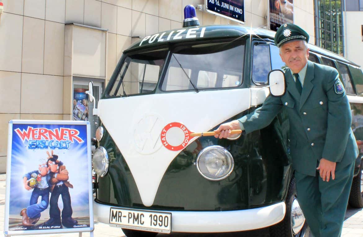 Der Polizei-Bulli mit dem Plakat zum neuen Werner-Film "Werner Eiskalt" vor dem Cineplex-Kino in Marburg mit Eberhard Dersch in historischer Polizeiuniform