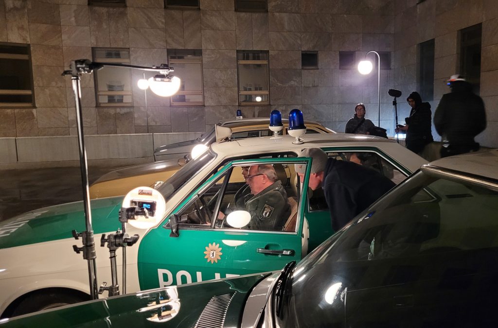 Letzte Anweisungen an den Polizisten Krasnick (Uwe Preuss) im Streifenwagen vor Drehbeginn, im Vordergrund ist der Marburger Opel Rekord D zu sehen