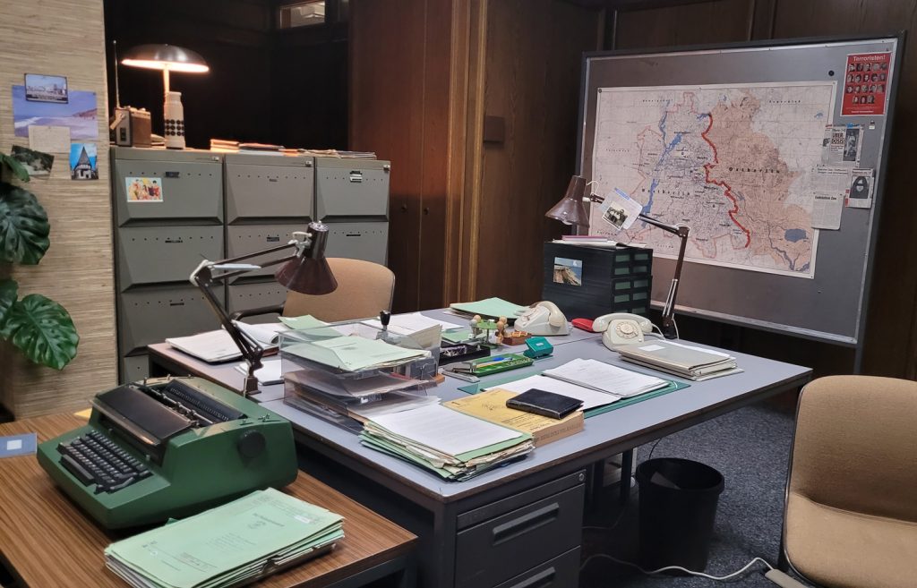 Eintauchen in die Vergangenheit, neben Schreibmaschinen auf den Bürotischen der Polizeidirektion hingen Zeitungartikel über Drogentote am Bahnhof Zoo und Fahndungsbilder von gesuchten RAF-Mitgliedern an der Wand, daneben eine Karte vom geteilten Berlin im Film Ku'damm 77