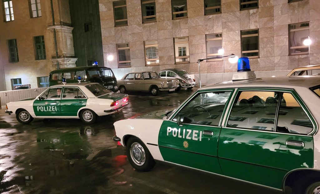 Die letzte Szene beim Dreh von Ku'damm 77, Polizist Krasnick fährt mit dem Streifenwagen zum Einsatz, im Vordergrund ist der Marburger Opel Rekord D zu sehen, hinten der VW T2 aus dem Polizeioldtimer Museum Marburg