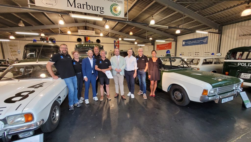 Gruppenfoto in einer der Hallen des Polizeioldtimer Museums Marburg mit den Vorstandsmitgliedern v. l. Tim Klingelhöfer, Barbara Sarama, Sebastian Sack (MdL), Martin Agel, Frank Dönges, Minister Timon Gremmels, Dirk Bamberger (MdL), Eberhard Dersch und Ruth Fischer (Stadt Marburg)
