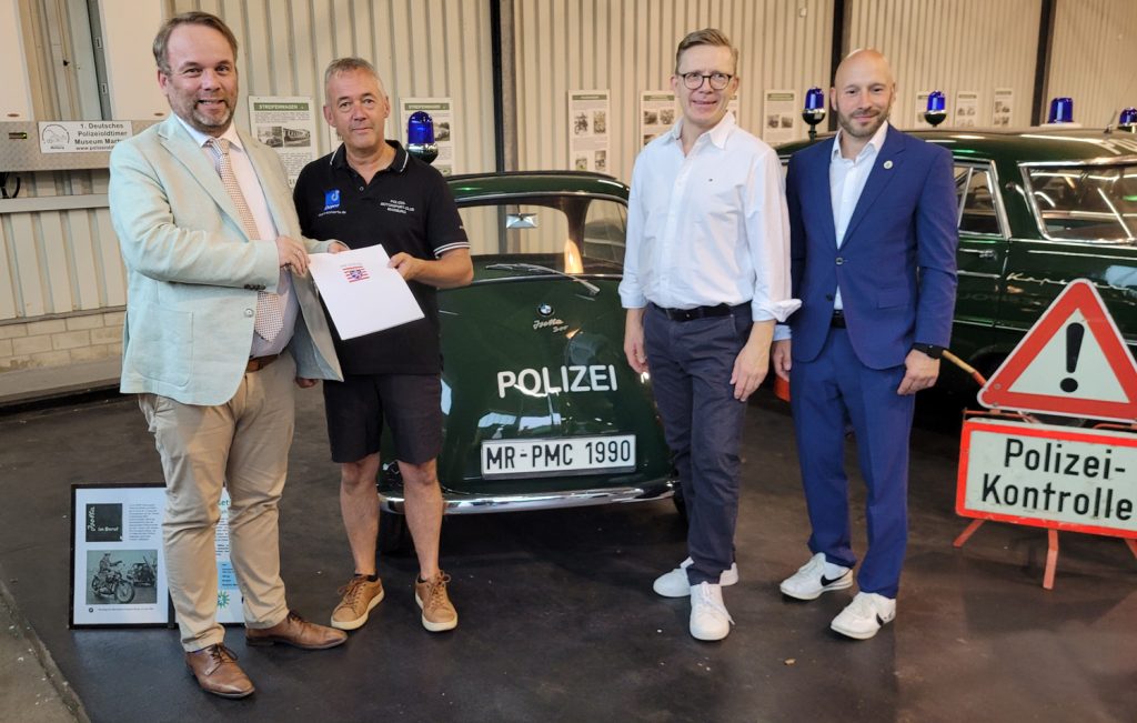 v.l. Kunst- und Kulturminister Timon Gremmels übergibt im Polizeioldtimer Museum Marburg den Förderbescheid für den Polizei-Motorsport-Club Marburg an den PMC-Vorsitzenden Frank Dönges – im Beisein von MdL Dirk Bamberger und MdL Sebastian Sack